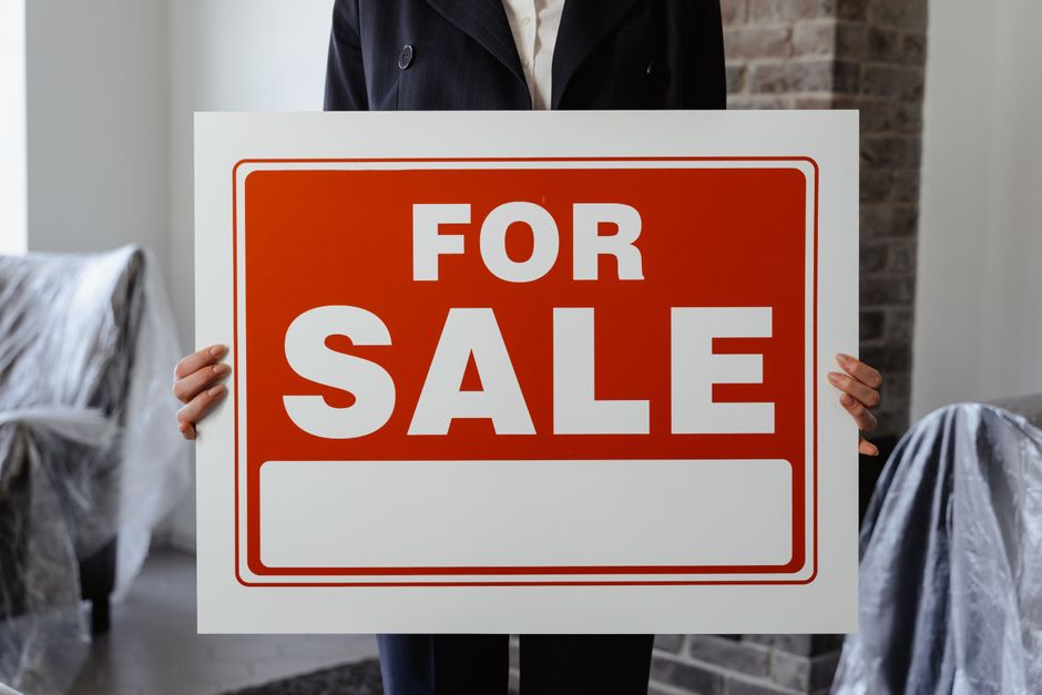A clean, modern 'For Sale' sign stands in the neatly manicured lawn of a suburban house, symbolizing the decision to list a property on the market.